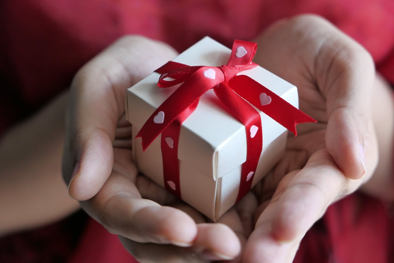 A heartfelt moment captured with hands holding a small gift box tied with a red ribbon.