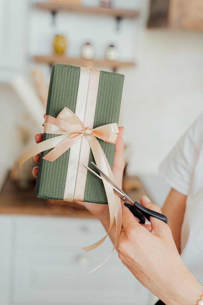 Hands wrapping a green gift box with a satin ribbon. Perfect for celebrations and seasonal gift-giving.