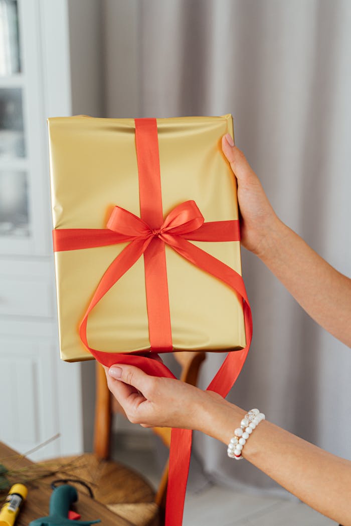 A beautifully wrapped gold gift with red ribbon held by hands, perfect for celebrations.